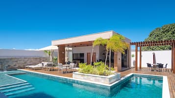 Un espace aménagé au bord de la piscine, comprenant un coin salon couvert, une piscine et une pergola ornée de plantes.