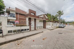 A modern building with a gated entrance, a sign for 'East Ville', and a paved street with a parked car. - Apartamento Moderno a 280m da Praia AST0103 (Porto Seguro)