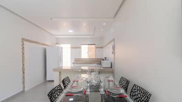 A modern kitchen with white appliances and a dining area with a glass table and black chairs.
