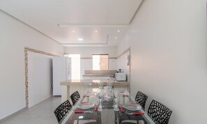 A modern kitchen with white appliances and a dining area with a glass table and black chairs. - Apartamento Moderno a 280m da Praia AST0103 (Porto Seguro)