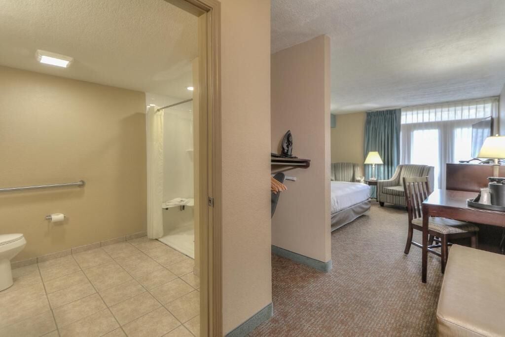 Camera d'albergo con doccia, bagno, letto, scrivania, sedia e un piccolo tavolo.