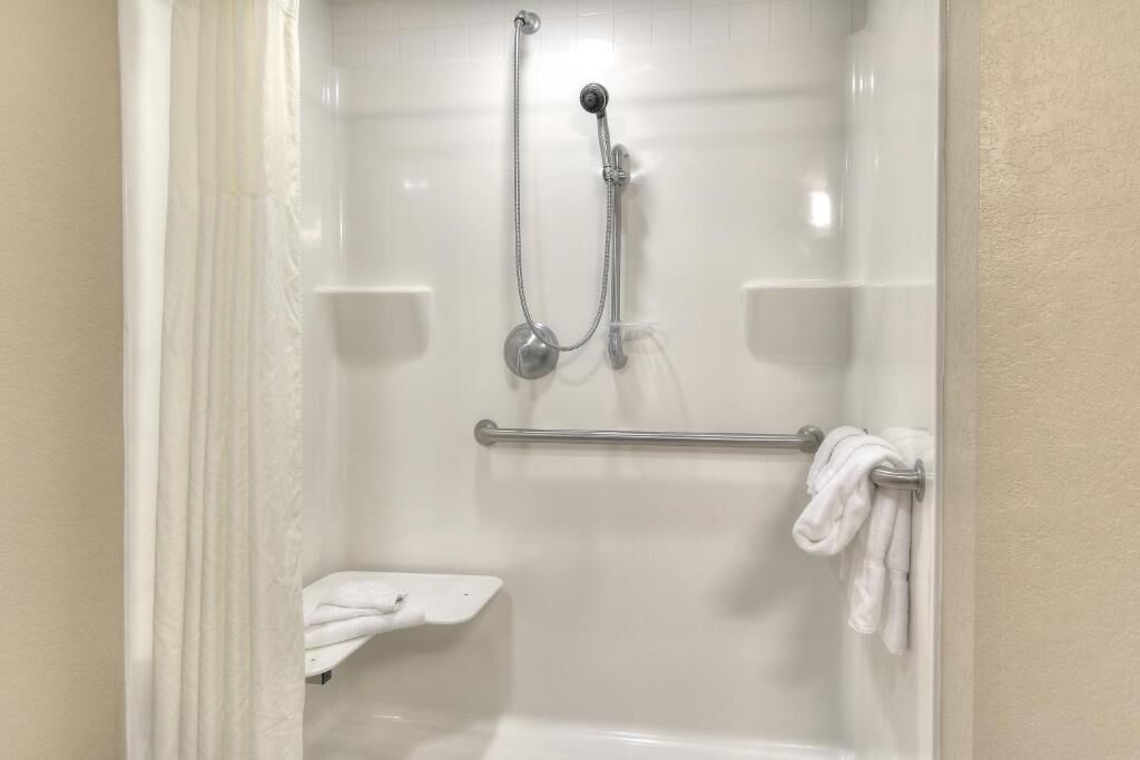 A shower with a handheld showerhead, a towel rack, and a small shelf.