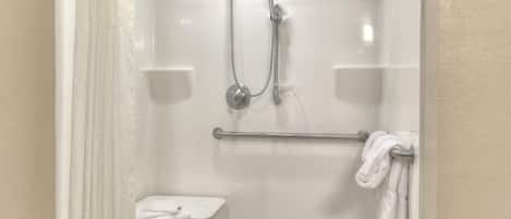 A shower with a handheld showerhead, a towel rack, and a small shelf.