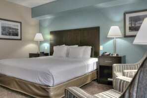 Quarto de hotel com uma cama grande, duas mesas de cabeceira, uma cadeira e uma mesinha de apoio com abajur.