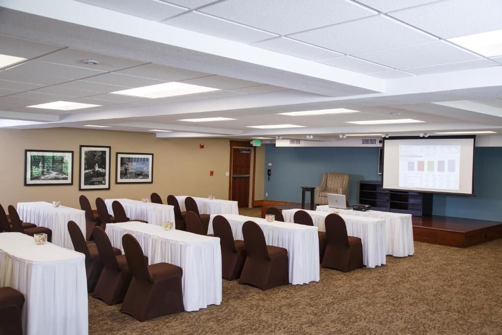 A conference room with tables and chairs, a projector screen, and framed pictures on the wall.