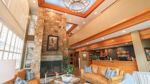 A spacious lobby with a stone fireplace, leather sofas, a wooden reception desk, and a chandelier.