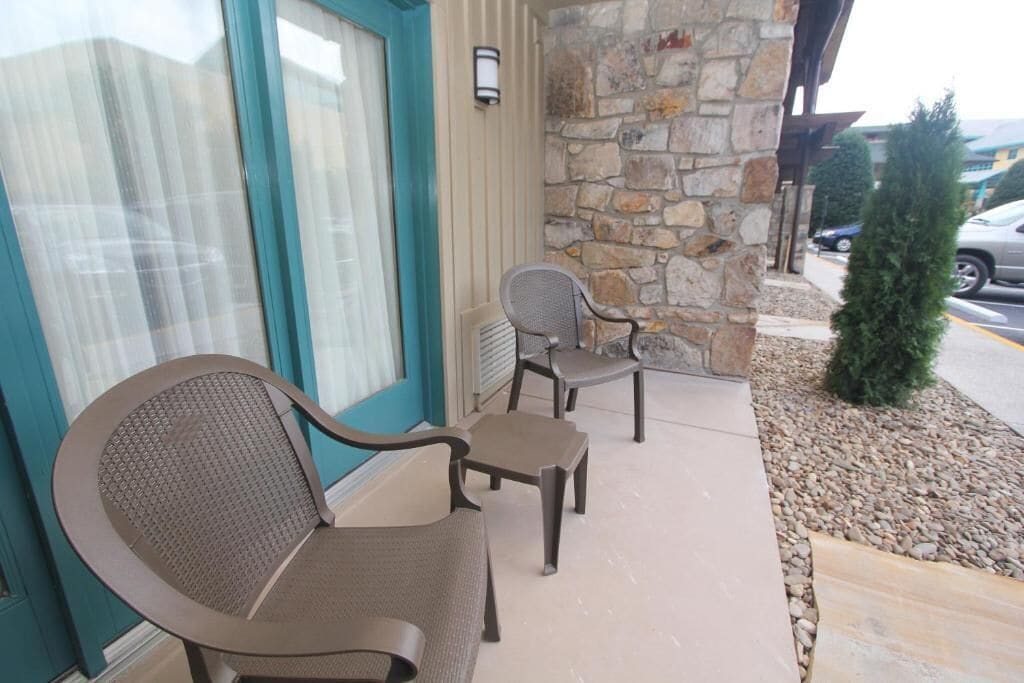 A patio area with two chairs and a small table, a stone wall, and a door with a window.