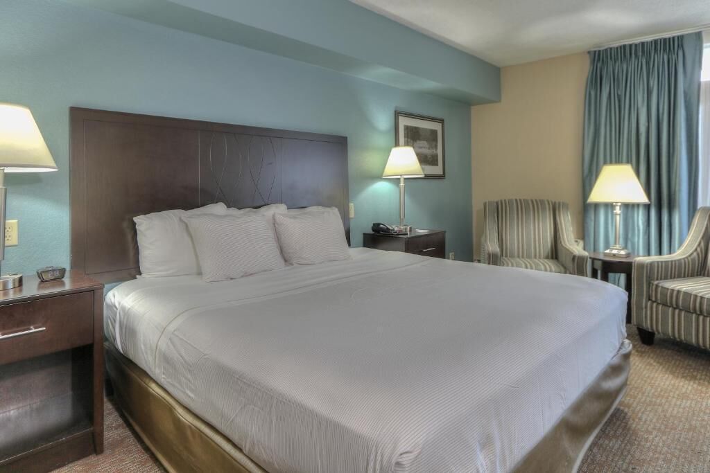 Ein Hotelzimmer mit einem großen Bett, zwei Nachttischen, einem Sessel und einer Lampe.