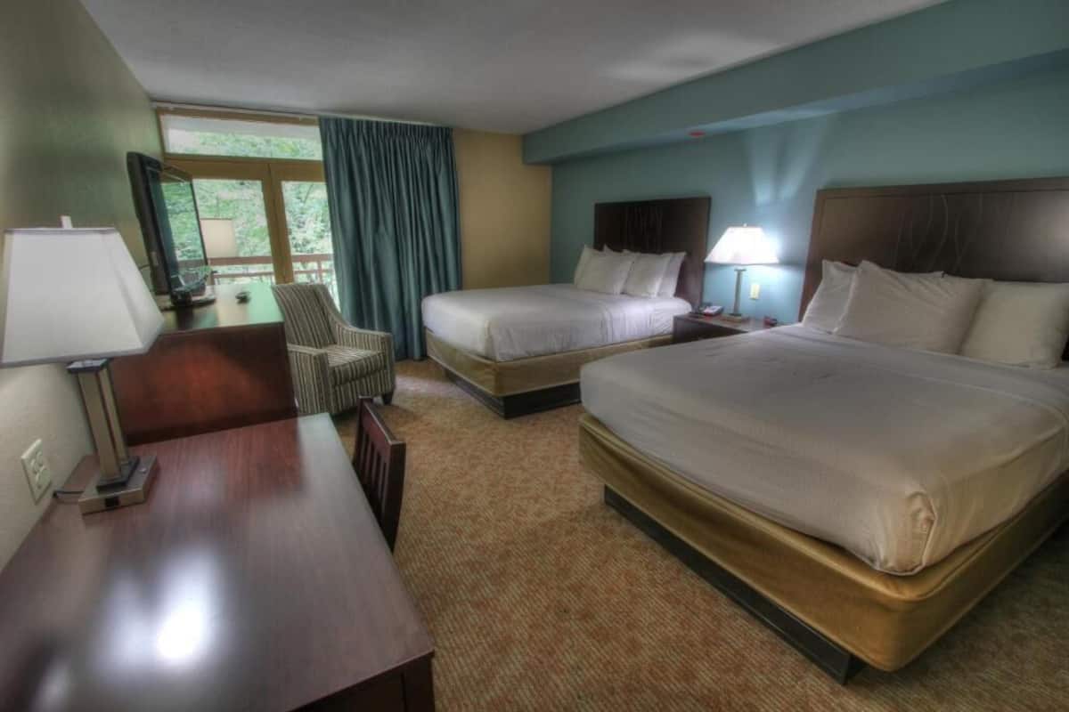 Habitación de hotel con dos camas, un escritorio, una silla y una ventana con cortinas.