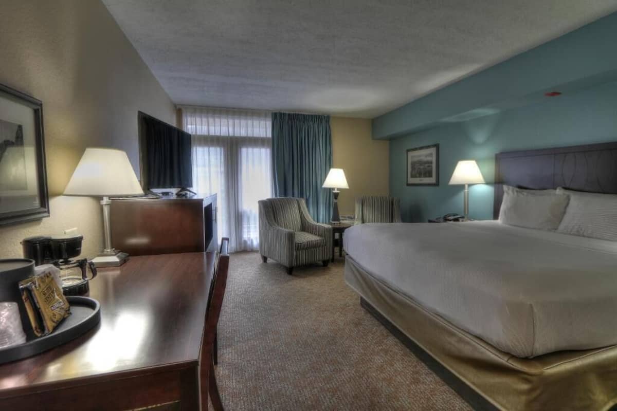Habitación de hotel con una cama grande, un escritorio con lámpara, una silla y un televisor.