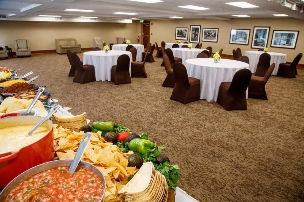 A banquet hall with round tables and chairs, buffet with various food items, and framed pictures on the walls.