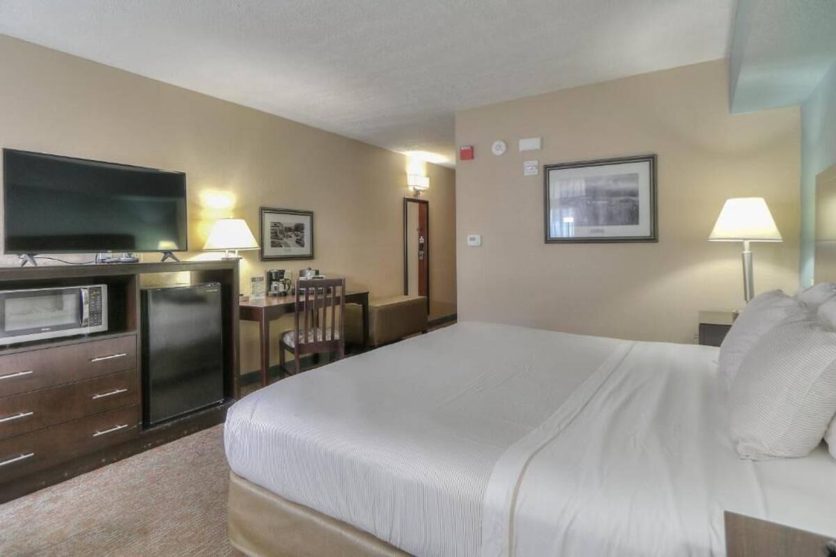 Habitación de hotel con una cama grande, televisión, escritorio con silla, microondas y refrigerador.