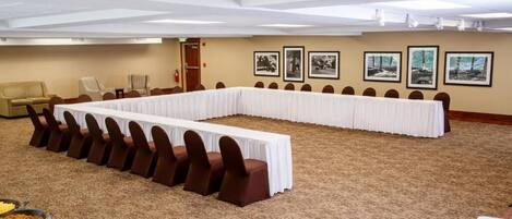 Un salón de conferencias con una larga mesa, sillas marrones y piso alfombrado.