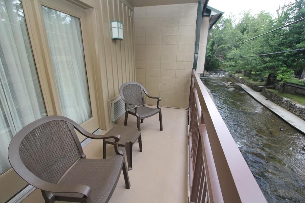 A balcony with two chairs and a table, overlooking a water feature and greenery.