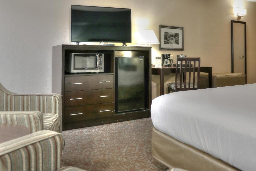 A hotel room with a bed, a television, a microwave, a refrigerator, a desk, a chair, and a coffee machine.