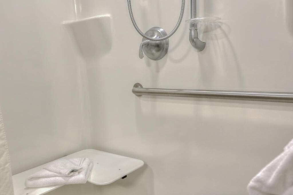 Une salle de bain avec une douche blanche, une barre d’appui et un porte-serviettes.