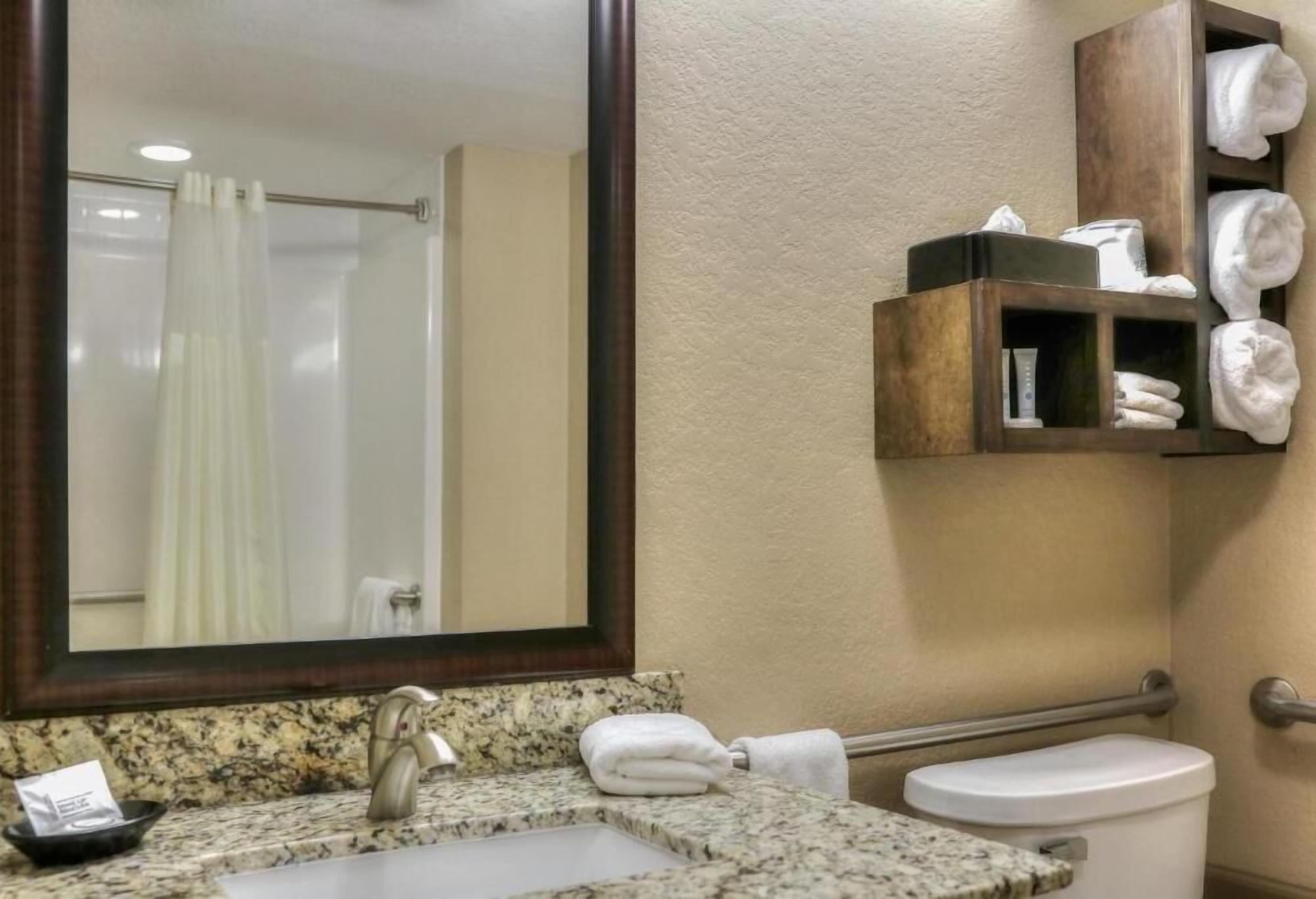 A bathroom with a granite countertop sink, a mirror, a towel rack, and a toilet.