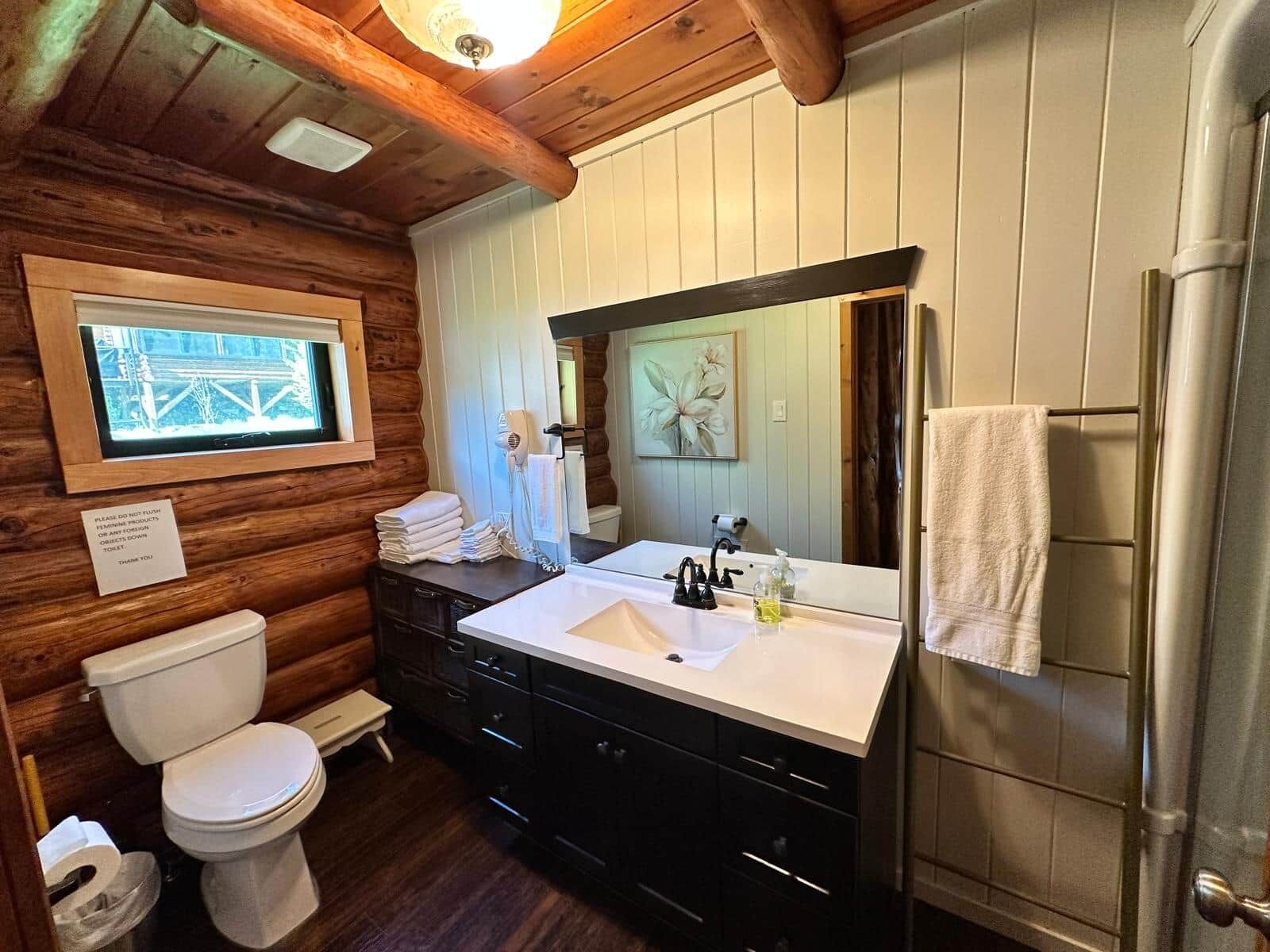 A wooden cabin bathroom with a toilet, sink, and a large mirror.