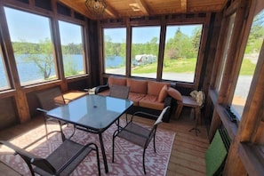 En stuga byggd av trä med en inglasad veranda, ett bord, stolar och en soffa med kuddar.