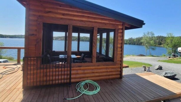 Eine Holzhütte mit einer Veranda, großen Fenstern und Seeblick.