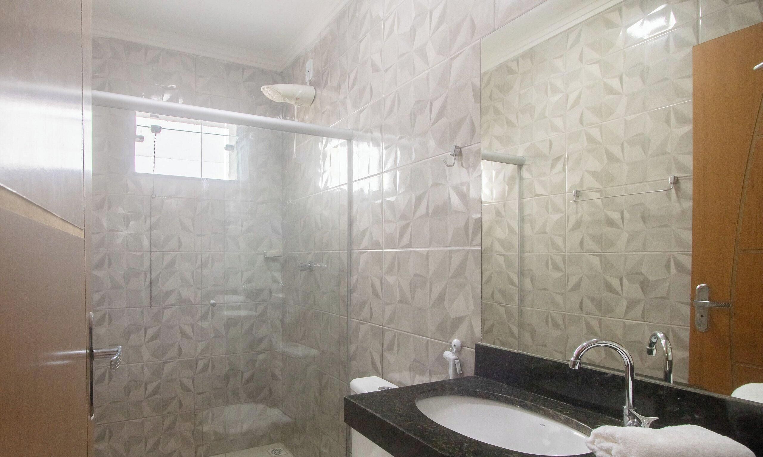 A bathroom with a glass shower enclosure, a sink with a mirror, and patterned tiles.