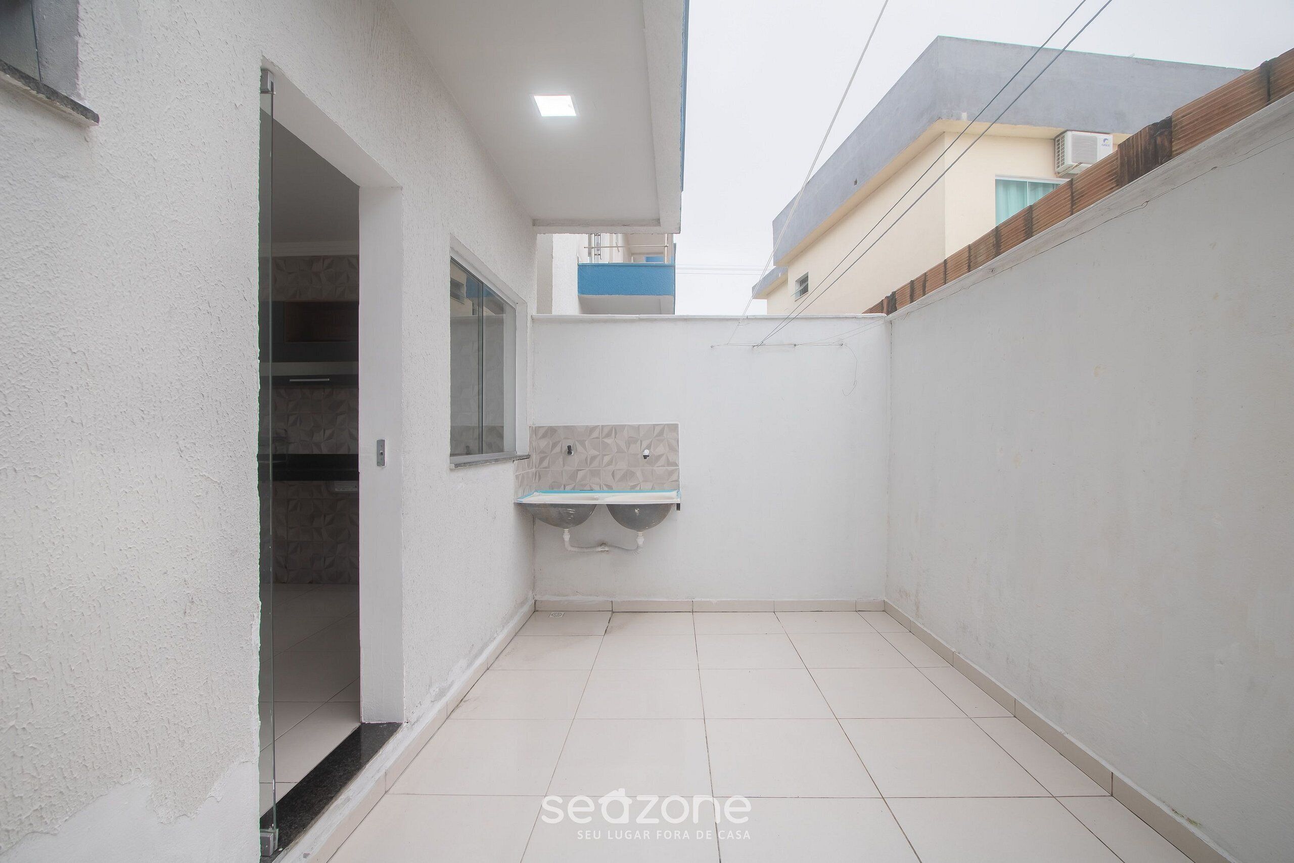 A narrow, enclosed outdoor space with a tiled floor, a small shelf, and a glass door leading to an interior room.