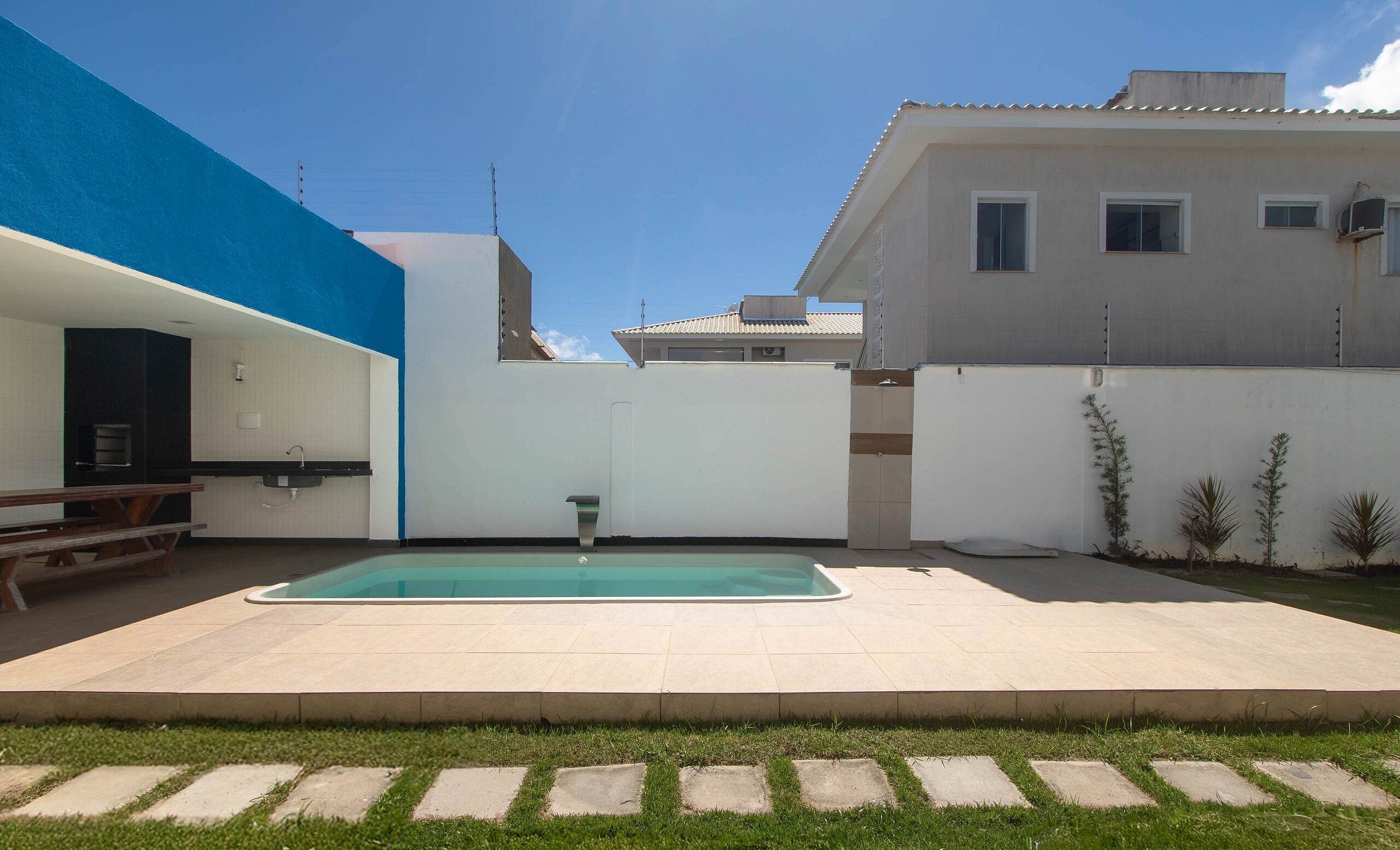 Un patio trasero con piscina, zona de barbacoa y un pequeño jardín.