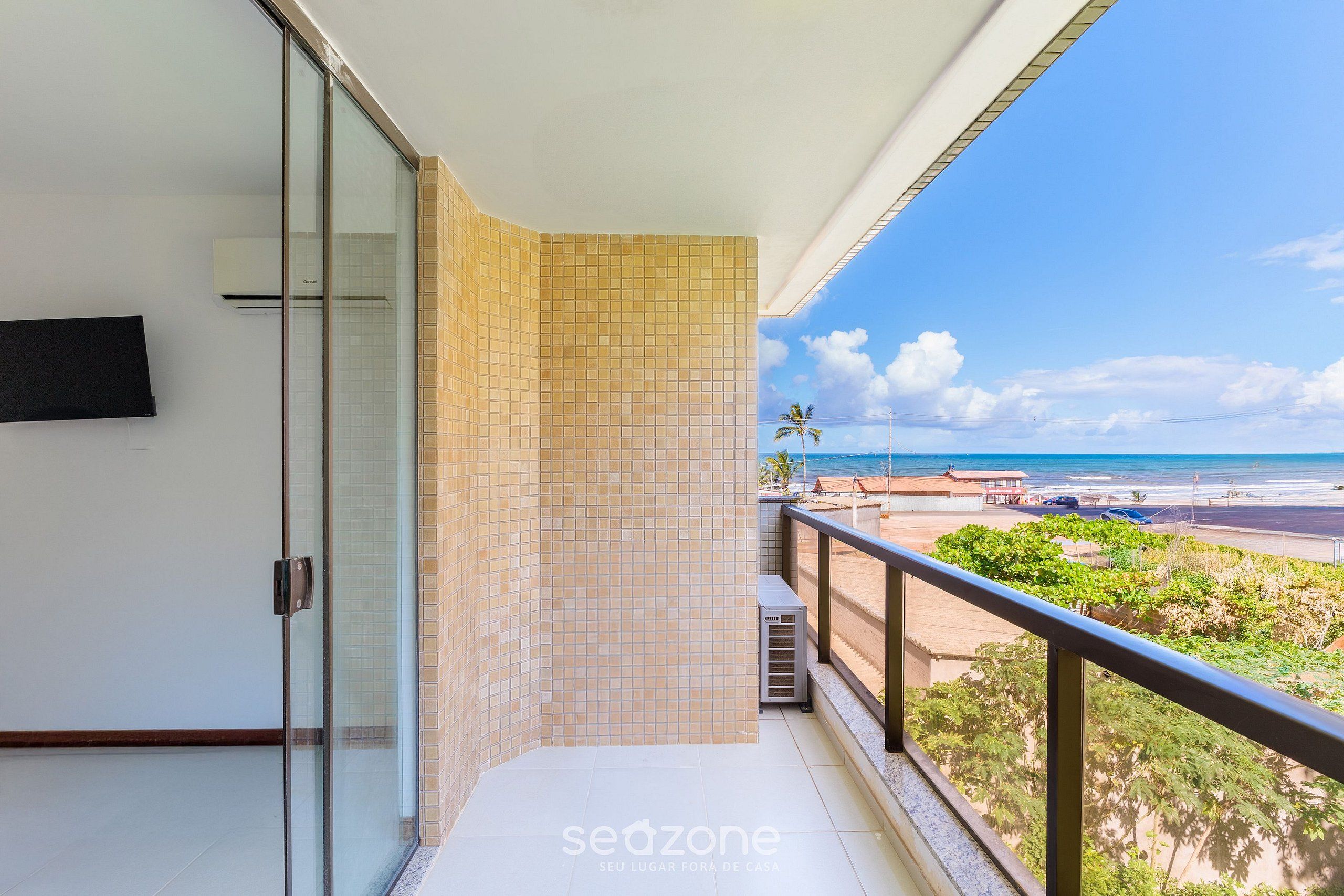 A balcony with a view of the beach, a glass door, and a tiled wall.