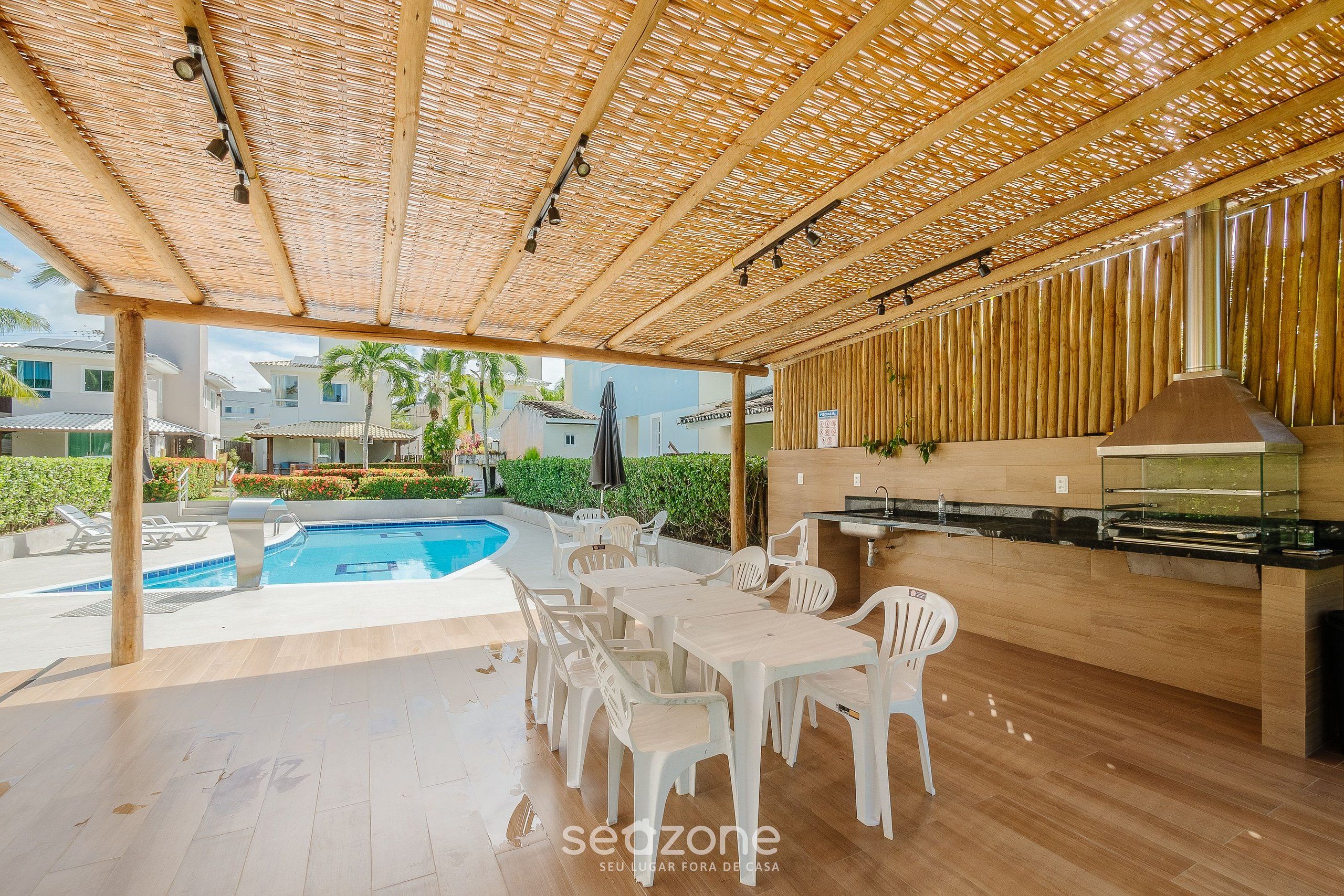 An outdoor patio with a pool, white plastic chairs, a wooden table, and a grill area.