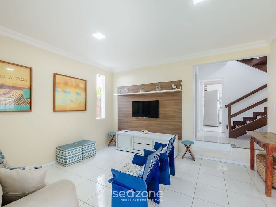 Una sala de estar con un sofá, un televisor fijado a una pared de madera y una escalera que sube a otro nivel.