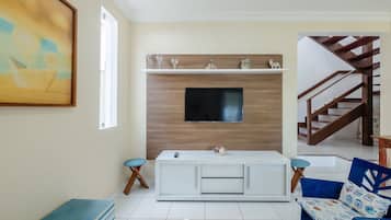 Una sala de estar con un televisor montado en una pared de madera, una consola blanca y un sofá azul con cojines estampados.