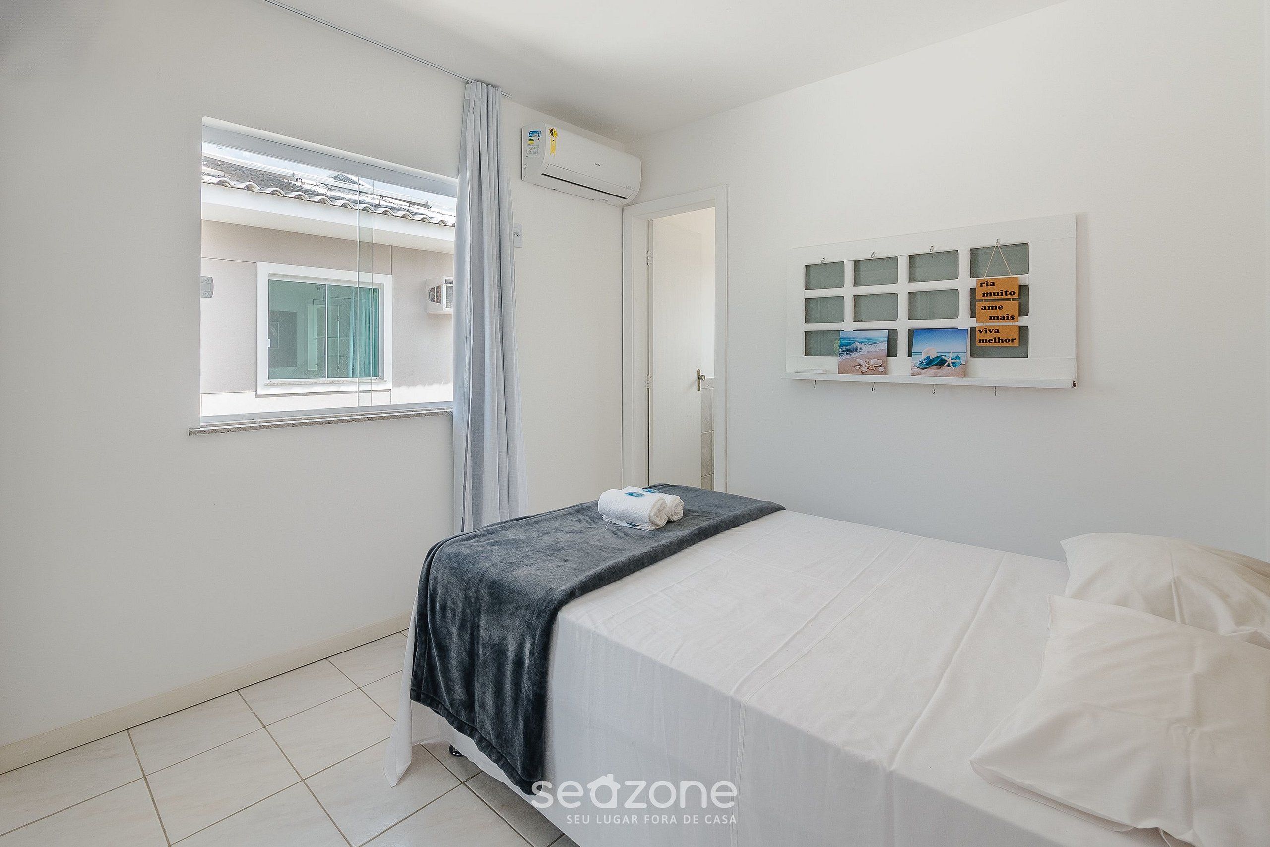 Un dormitorio con cama, ventana, equipo de aire acondicionado y una pantalla montada en la pared.