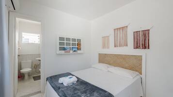 Un dormitorio con cama, ventana, estante con artículos de aseo e cabecero.