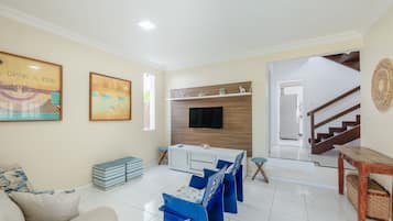 Una sala de estar con un sofá, un televisor fijado a una pared de madera y una escalera que sube a otro nivel.