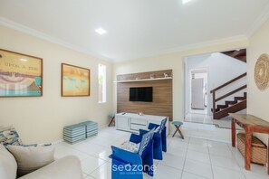 A living room with a sofa, a television mounted on a wooden wall, and a staircase leading to another level. - Spacious House w/ Pool in Guarajuba Cag0003 (Camaçari)