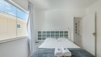A hotel room with a bed, a nightstand, a window with curtains, and a view of the outside.