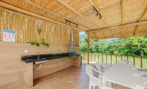 An outdoor kitchen area with a grill, a sink, and a table with chairs. - Spacious House w/ Pool in Guarajuba Cag0003 (Camaçari)