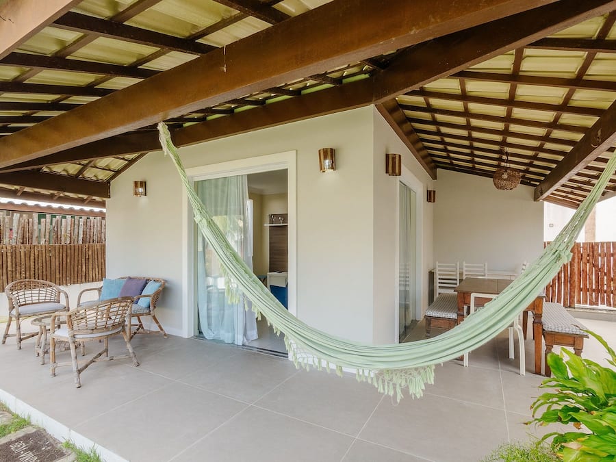 Une terrasse couverte avec un hamac, des meubles en osier et une vue sur l’intérieur.