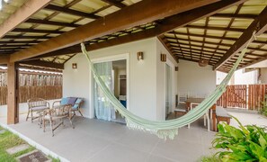 Un patio cubierto con una hamaca, muebles de mimbre y vistas al interior.