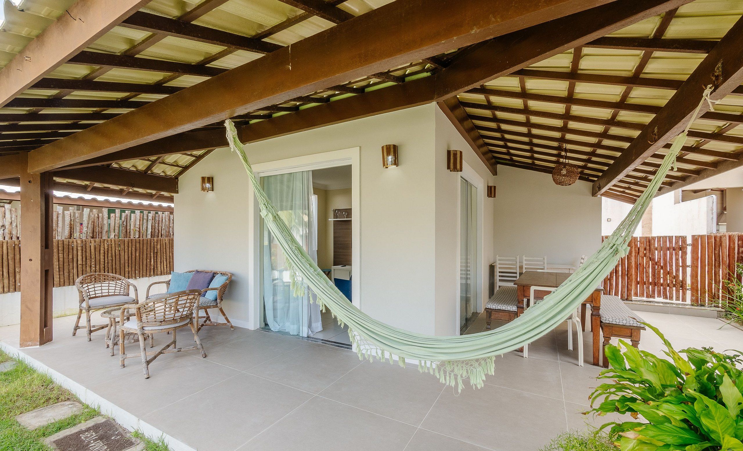 A covered patio with a hammock, wicker furniture, and a view of the interior.
