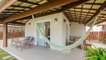 A covered patio with a hammock, wicker furniture, and a view of the interior.