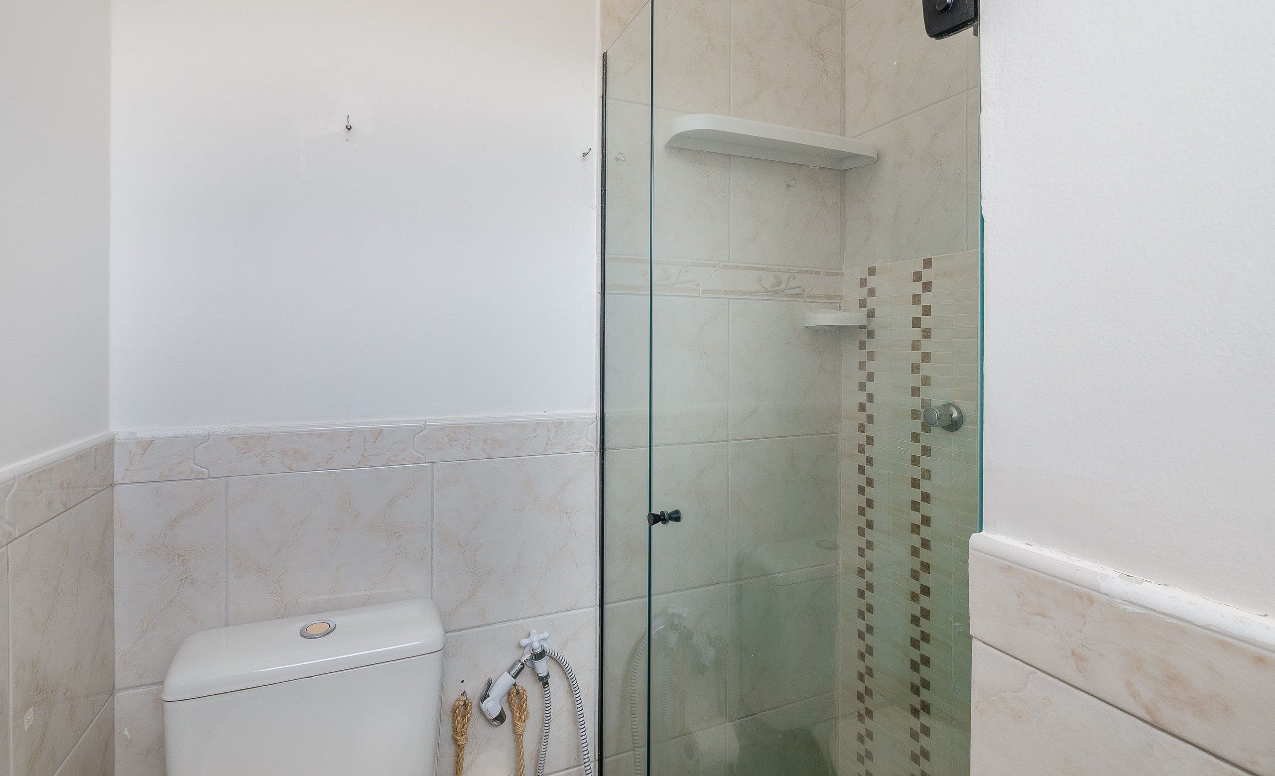 Casa de banho com chuveiro separado por vidro, sanita e barra para toalhas.