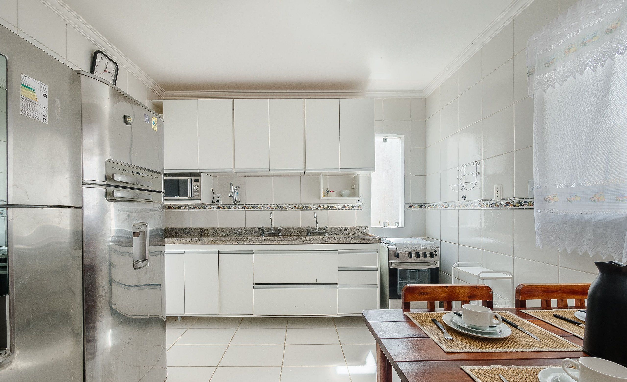 Una cocina moderna con armarios blancos, electrodomésticos de acero inoxidable y un comedor con sillas de madera y una mesa.