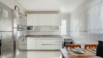 Una cocina moderna con armarios blancos, electrodomésticos de acero inoxidable y un comedor con sillas de madera y una mesa.