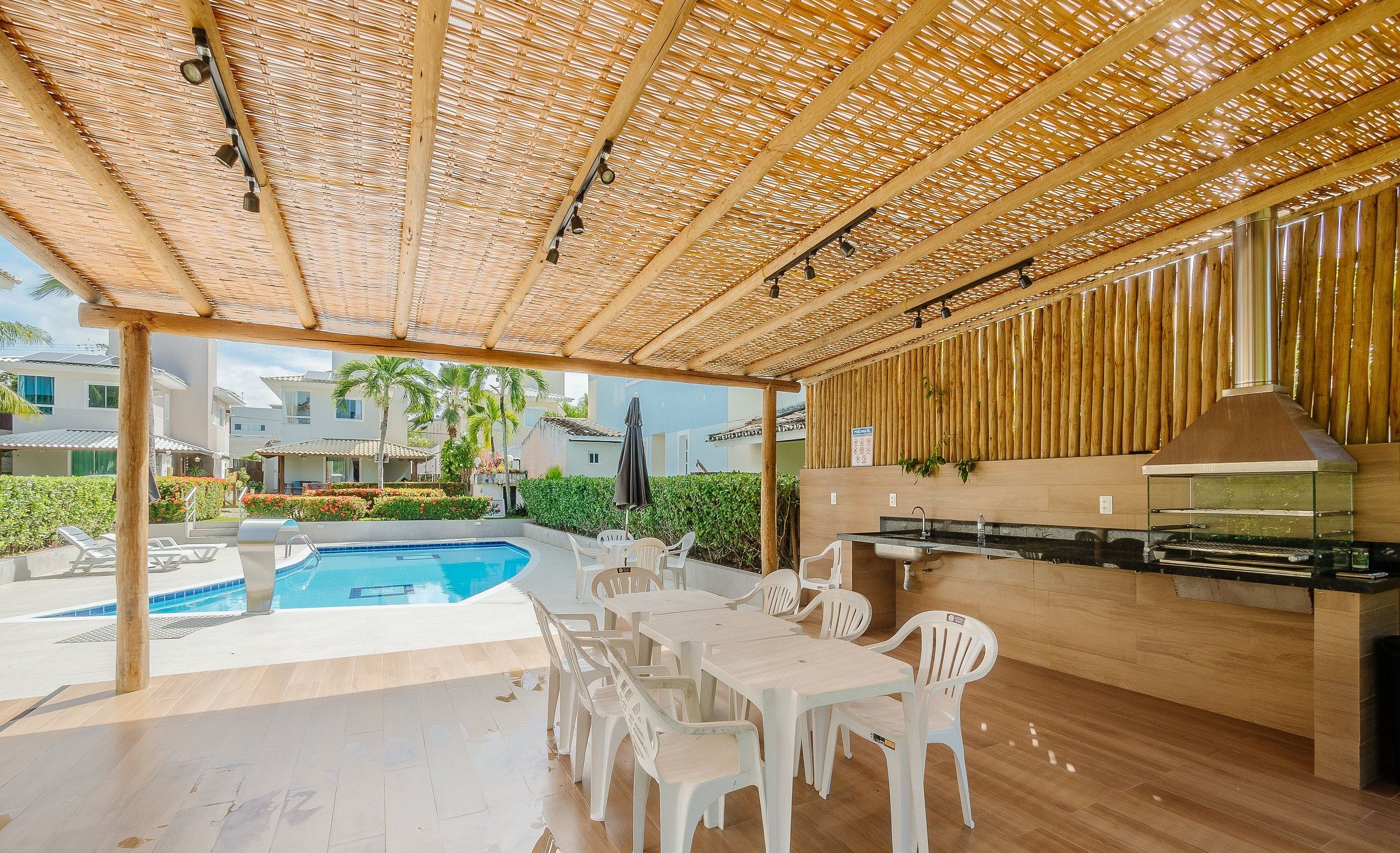 Un patio exterior con piscina, sillas de plástico blanco, una mesa de madera y zona de barbacoa.