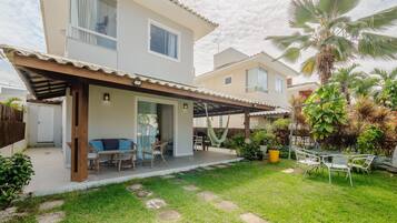 A two-story house with a covered patio, outdoor seating, and a well-maintained garden with palm trees and potted plants.