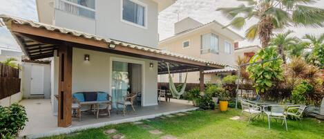 A two-story house with a covered patio, outdoor seating, and a well-maintained garden with palm trees and potted plants.