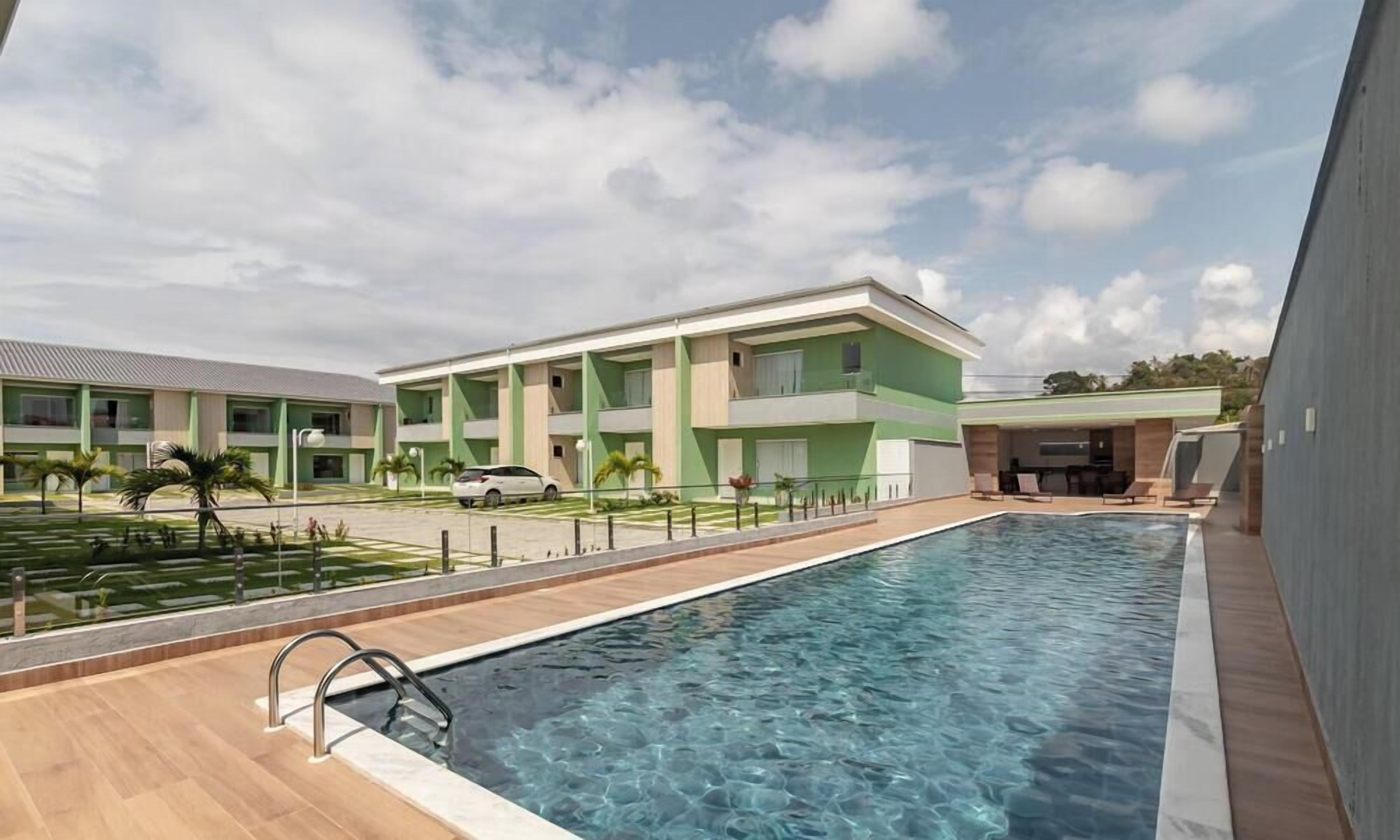 Ein Pool mit Holzterrasse, ein grünes Gebäude mit mehreren Balkonen und einem wolkenlosen Himmel.