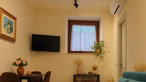 A compact living space with a dining area, a sofa, a TV mounted on the wall, and a window with a curtain.