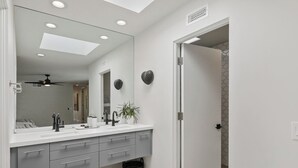A modern bathroom with a large mirror, a ceiling fan, recessed lighting, and a shower area. - GATED, Spacious 2-bedroom condo in Indian Wells close to restaurants and more. (Indian Wells)